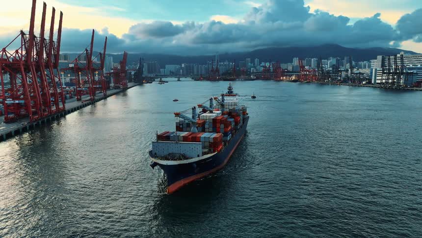 Aerial of a loaded cargo ship moving on water body surface close to a shipping dock during daytime