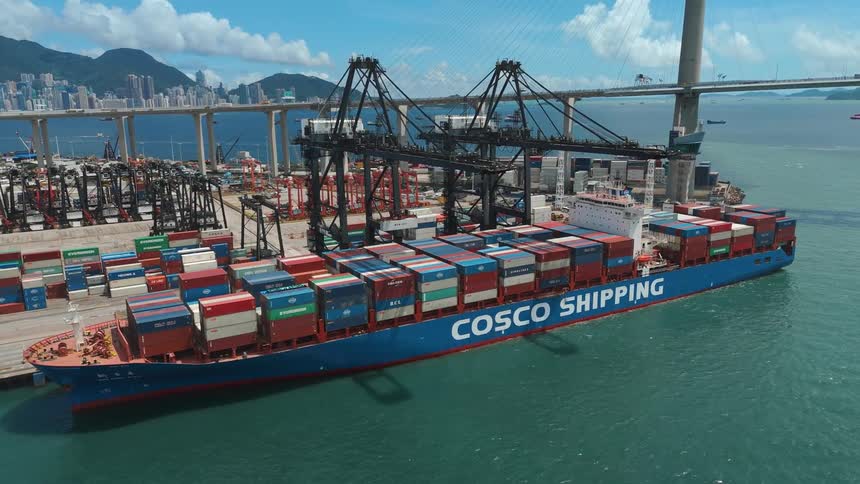 Container ship sits at a loading dock near the loading cranes while vehicles travel across a bridge in the background