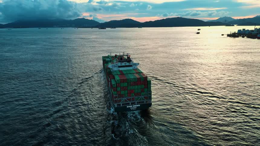 Cargo ship loaded with containers sailing at sea during sunset