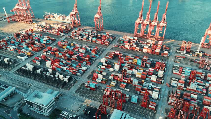 Aerial view of a port with cranes and hundreds of colorful containers arranged in rows