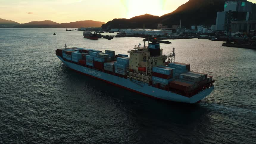 Maersk cargo ship sailing near a port city and bridge