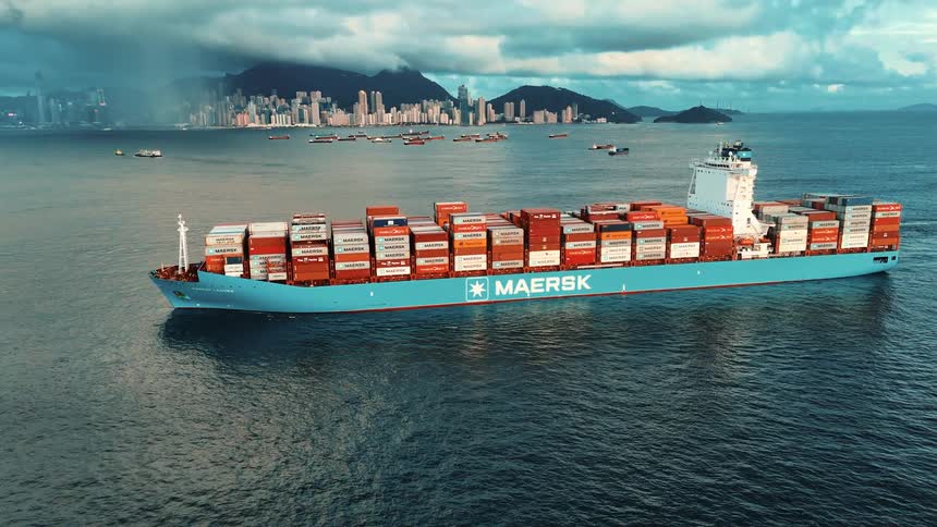 Maersk cargo ship carrying colorful containers at sea with a coastal city in the background