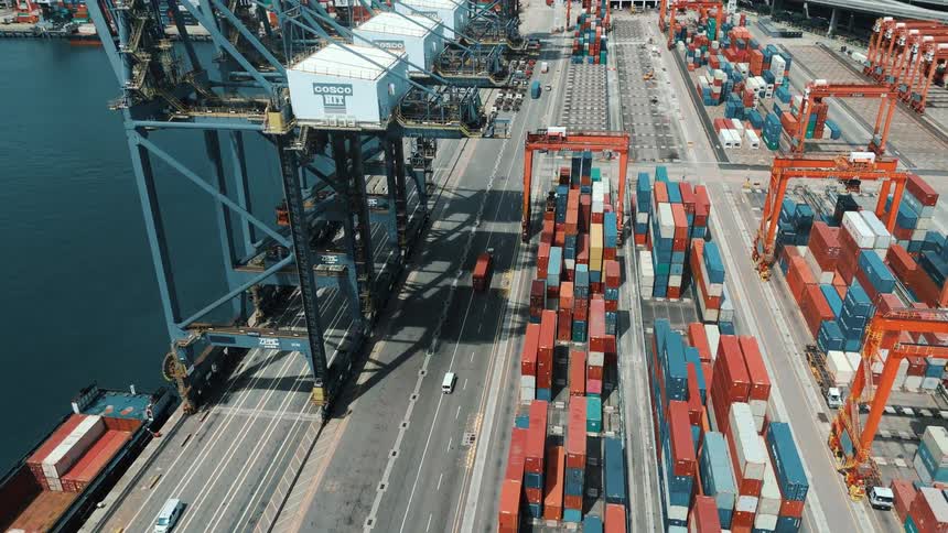 Colorful containers stacked in a port terminal with cranes and vehicles moving along the cargo lanes