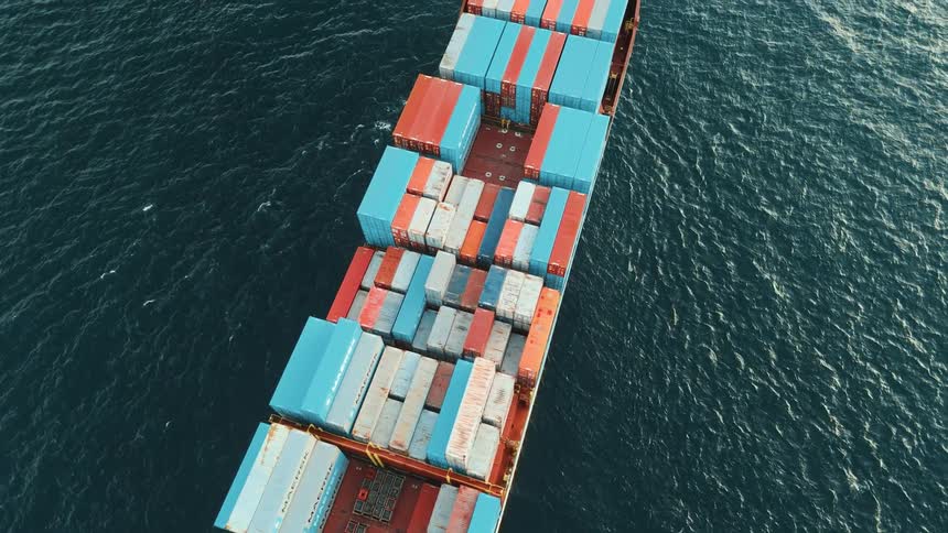 Cargo ship seen from above carrying blue red and white containers in open sea