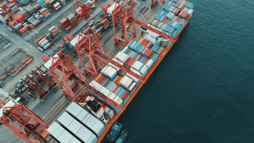 Cargo ship docked at port being loaded with containers by red cranes