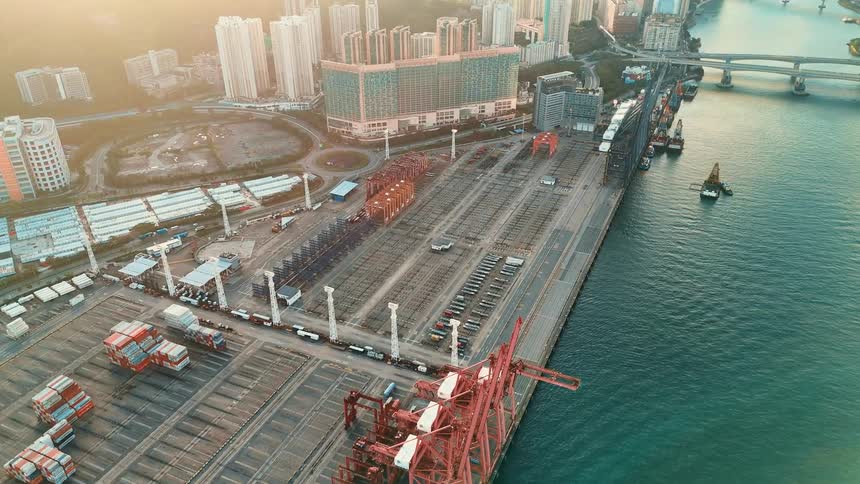 A seaport with one section empty and another filled with containers at midday with the city view in the background