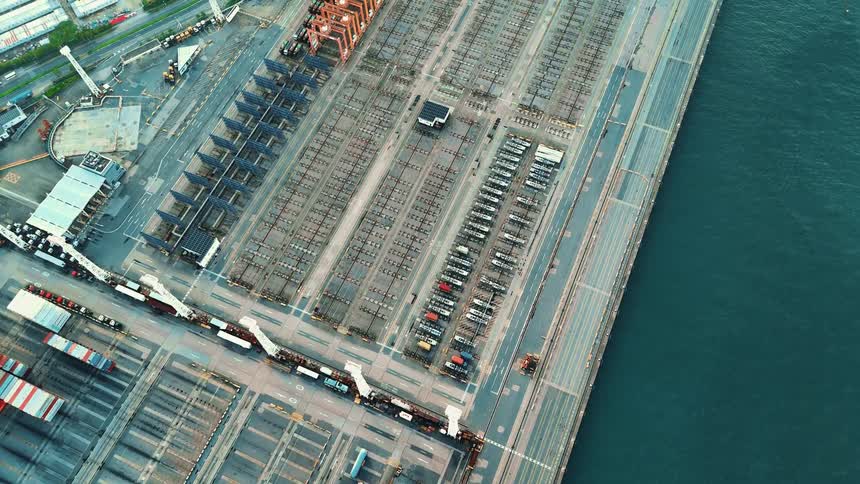 Aerial view of a port with orange cranes and large yard areas nearly empty near the sea