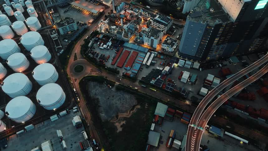 Night aerial view of an industrial area with white storage tanks warehouses and illuminated buildings next to an expressway