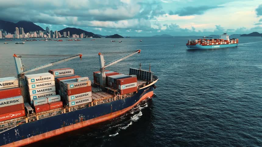 A cargo ship loaded with maersk containers sails through coastal waters as another approaches in the distance