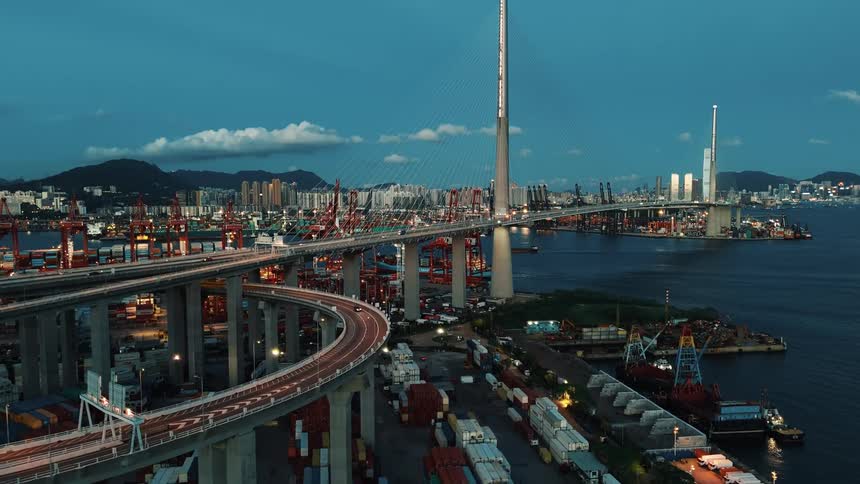 Cablestayed bridge lit at dusk over the port with containers