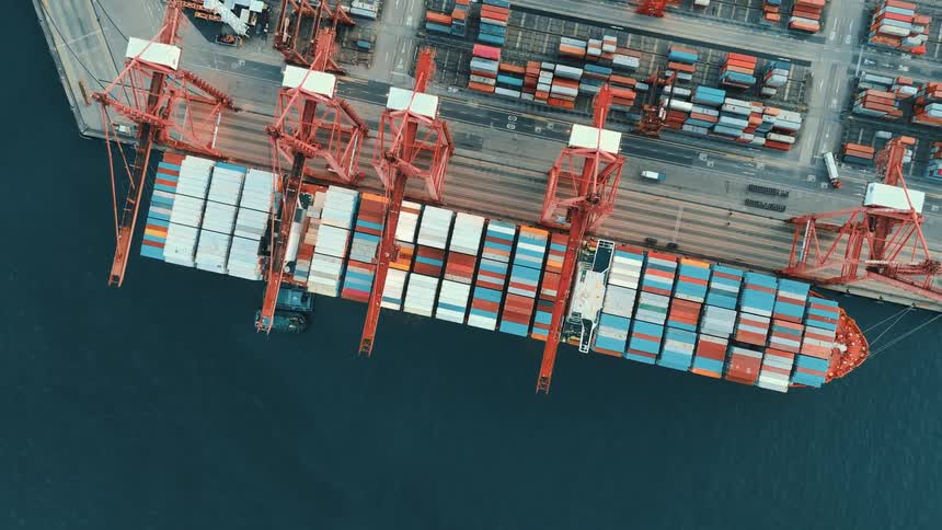Aerial view of a cargo ship being loaded with colorful containers by cranes at the port