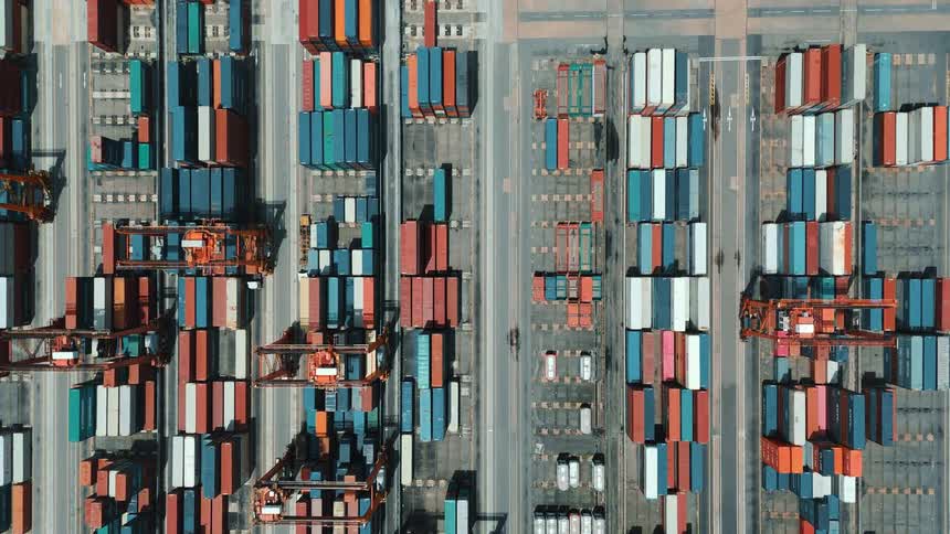 Roads allow passage between multiple rows of stacked shipping containers during the daytime