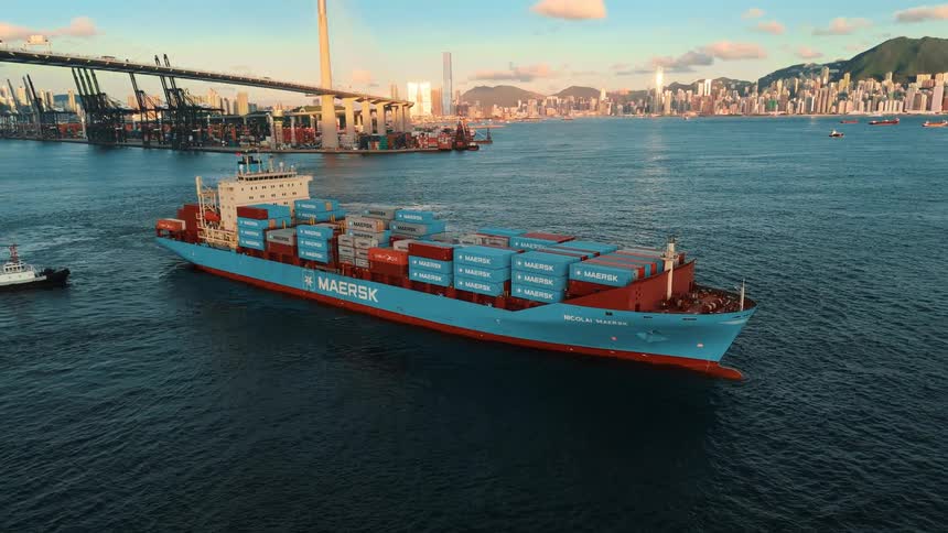 Maersk cargo ship carrying containers at sea with a city and mountains in the background