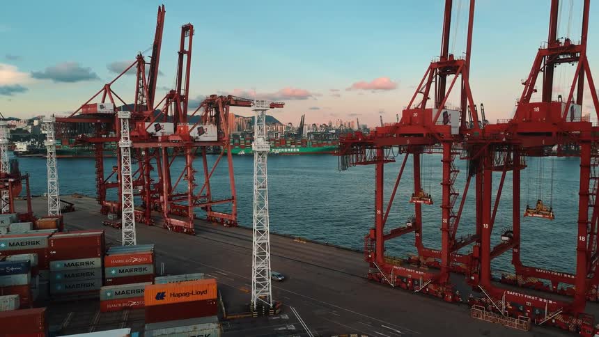 View of cranes and stacked containers at a port near the sea