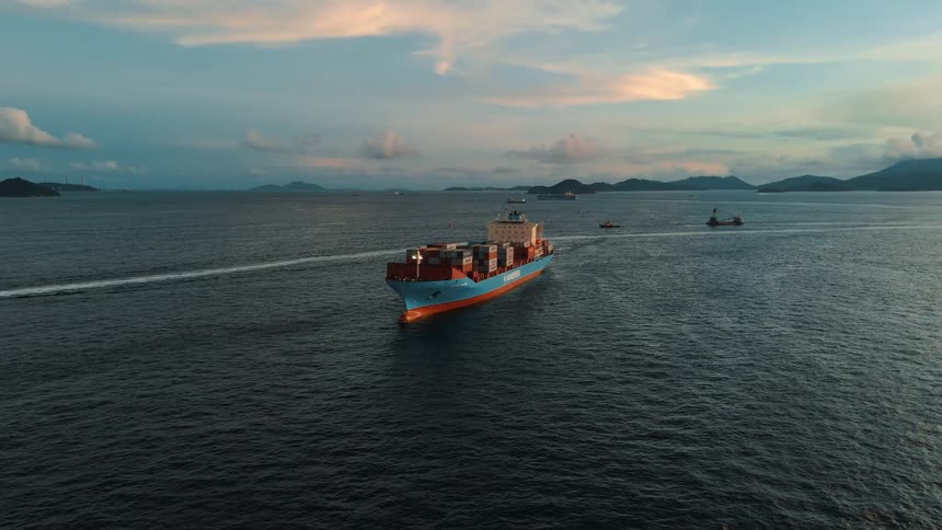 Maersk cargo ship sailing at sea with containers on board and mountains in the background