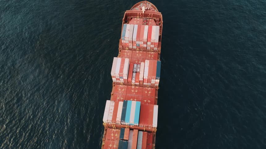 Red cargo ship carrying colorful containers at sea