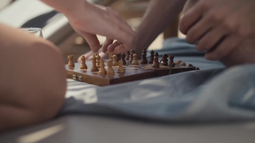 Two people are playing a game of chess on a small wooden board placed on a blanket