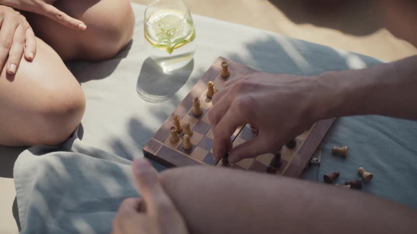 Two friends on a blanket outdoors play a game of chess
