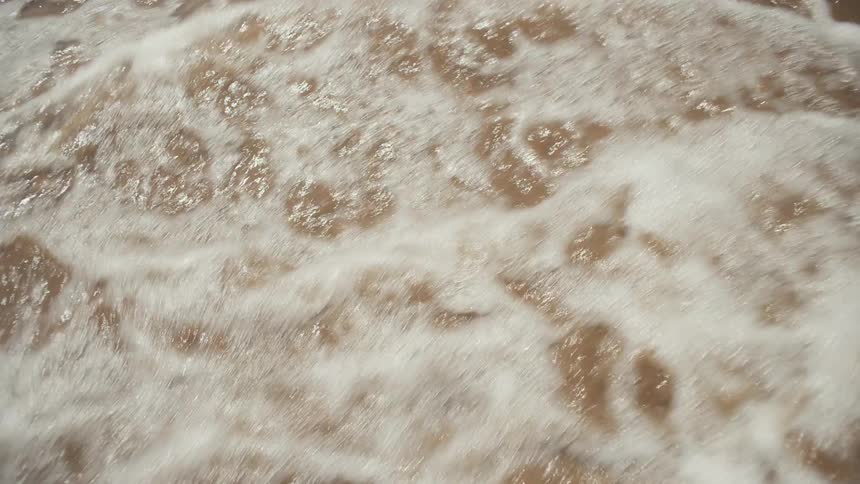 Gentle waves roll onto a sandy beach the foamy water recedes leaving the wet sand glistening in the sun