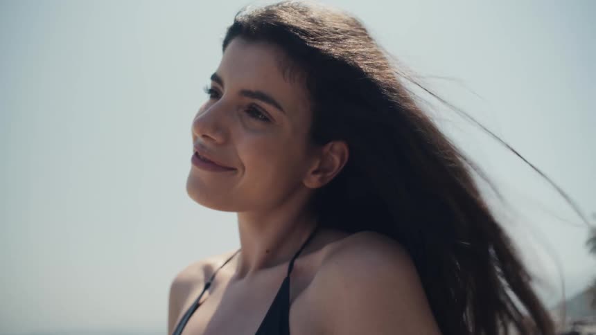 A woman is outside smiling as her long hair blows in the wind