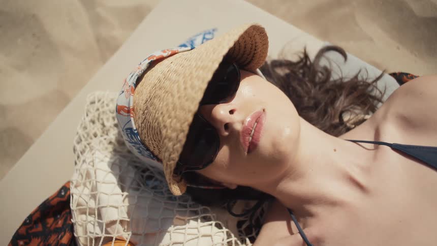 Woman wearing a straw hat and sunglasses resting on a beach lounger