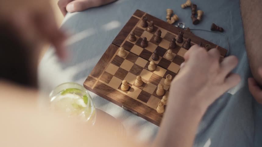 Two people playing chess on a wooden board while drinking a cocktail