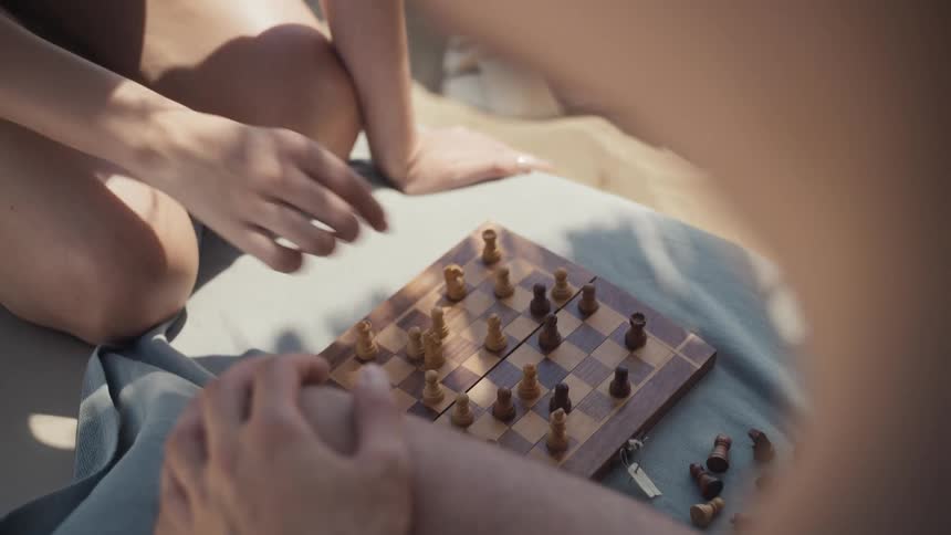 Person moving a piece on a chessboard while playing at the beach