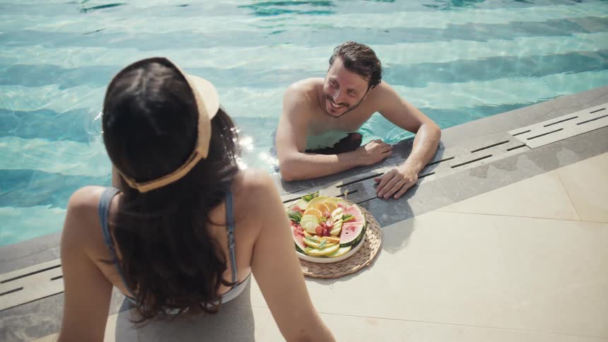 Man and woman enjoy a relaxing moment by the pool with fruits nearby