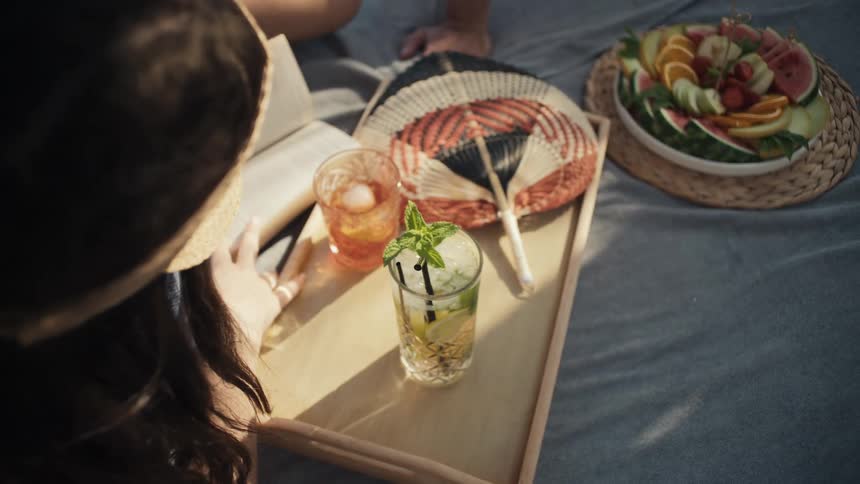 A couple is enjoying a relaxing day by the pool on a wooden tray there are refreshing drinks and a large platter of fresh fruit