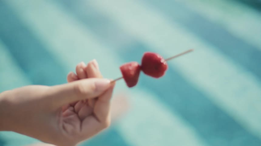Woman holds a thin stick with two strawberry halves over a pool