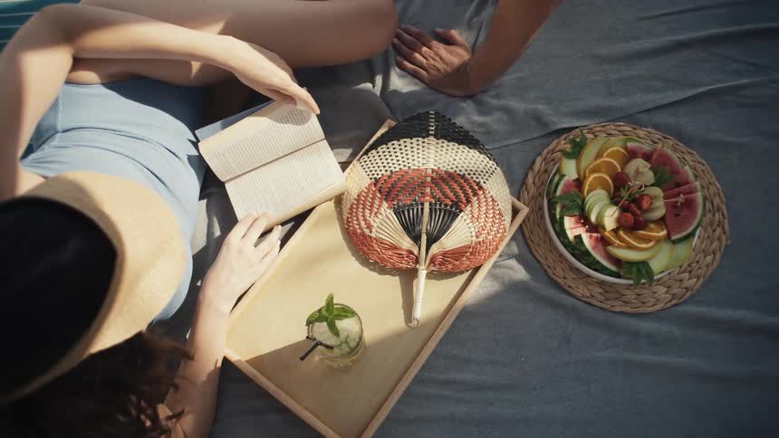 Couple enjoys a picnic with drinks and a plate of fresh fruits on the blanket