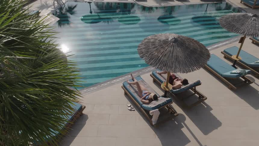 Two people relax on lounge chairs by a sunny pool