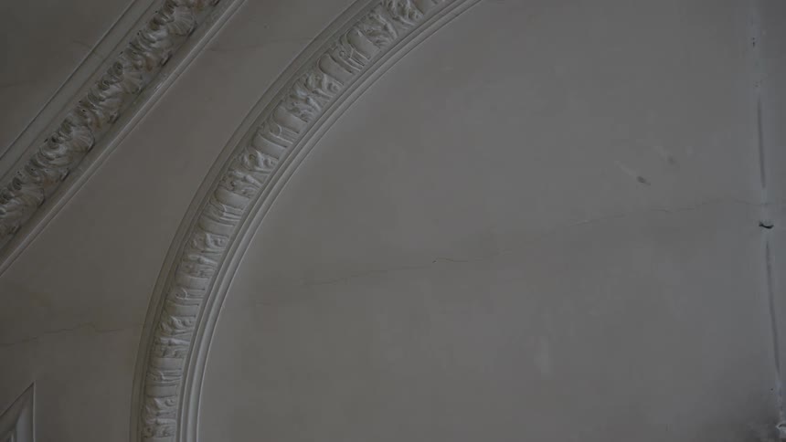 A closeup shows a patterned ornate ceiling with arched molding the ceiling appears to be old with some cracks visible in the plaster