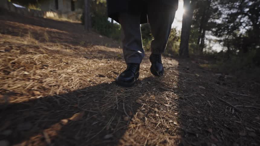 Person walks along a shaded dirt trail wearing black boots