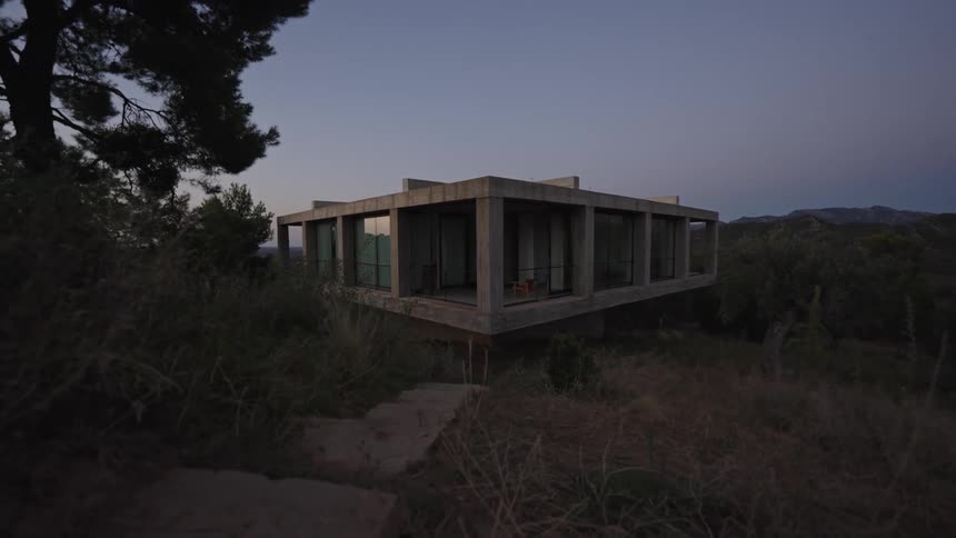 Modern concrete house with large glass windows surrounded by vegetation
