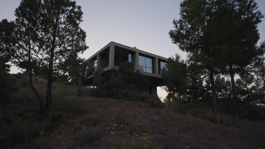 Modern concrete house with large glass windows located among trees