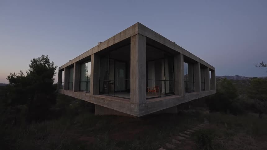 The video shows a concrete and glass house perched on a hillside at dusk the building has a modern minimalist design with large windows providing a view of the surrounding landscape