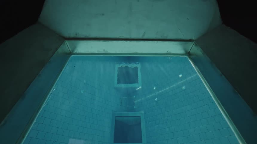 Sunlight streams through square windows into a serene tiled pool viewed from beneath the surface