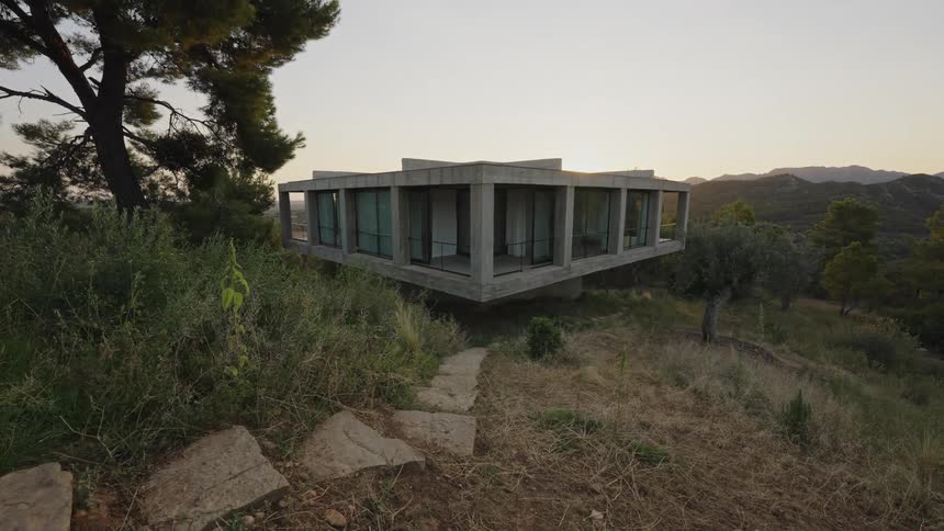 Elevated concrete house with large glass windows in a mountainous landscape