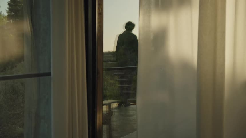 Person stands on a balcony behind a glass door