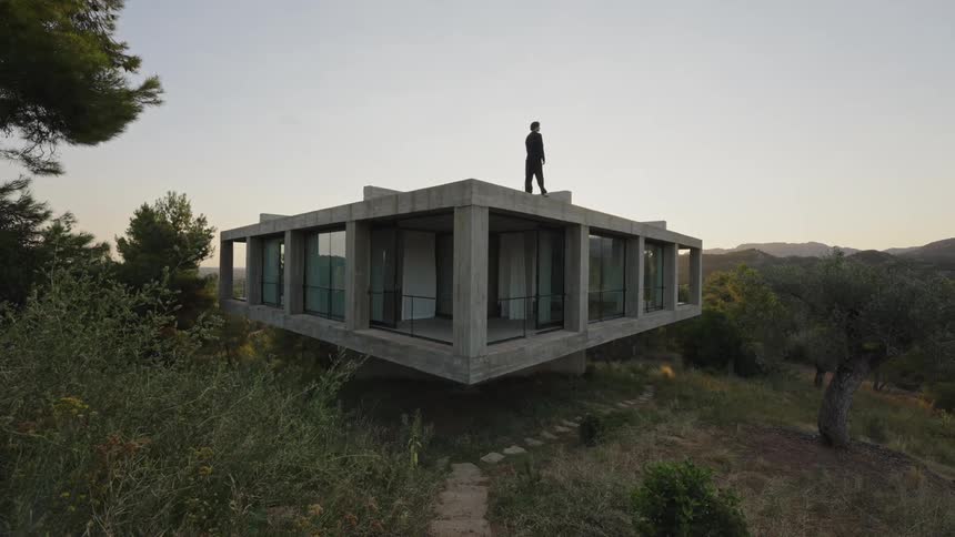 A person walks on the roof top of a concrete house with window walls