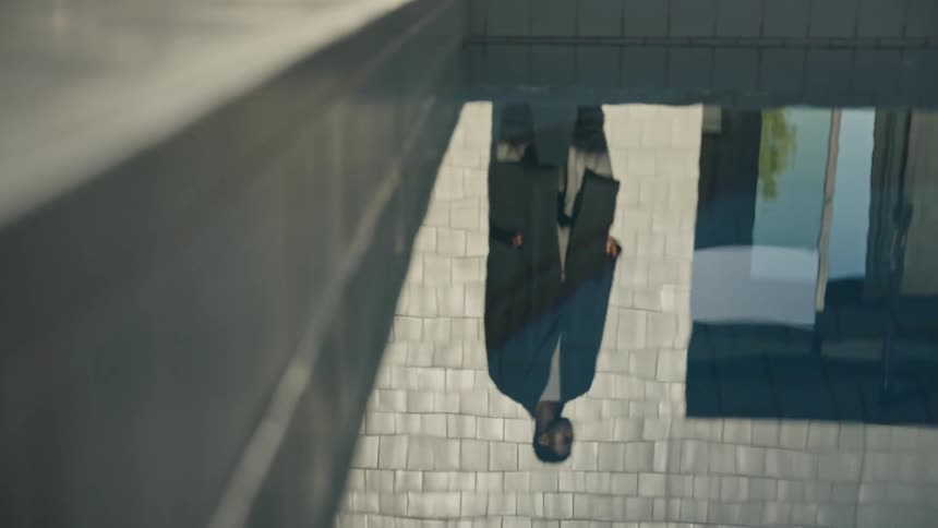 Reflection of a standing person captured in the water beside a building