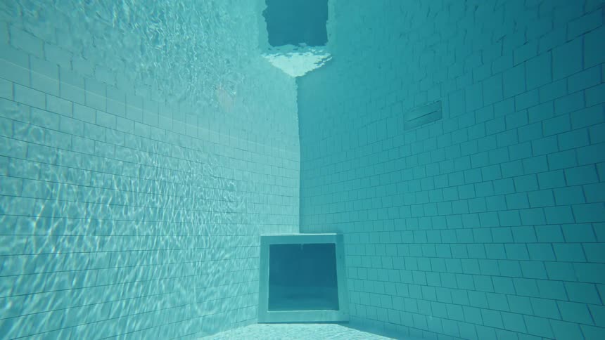 The video shows a unique perspective from underwater inside a swimming pool the camera is positioned looking up towards the surface of the water and a square window on the pools bottom