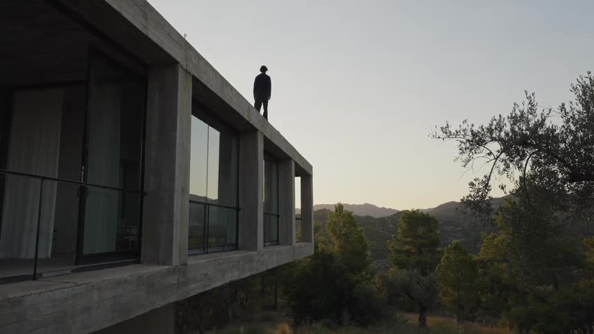 Person walks along the edge of the roof of a concrete house in a forest