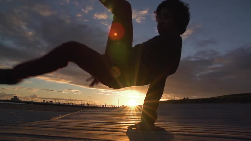 A person break dancing at sunset on a cloudy day