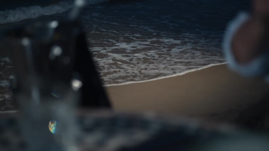 Someone is holding a glass and dirinking wine on a seaside where waves are crashing