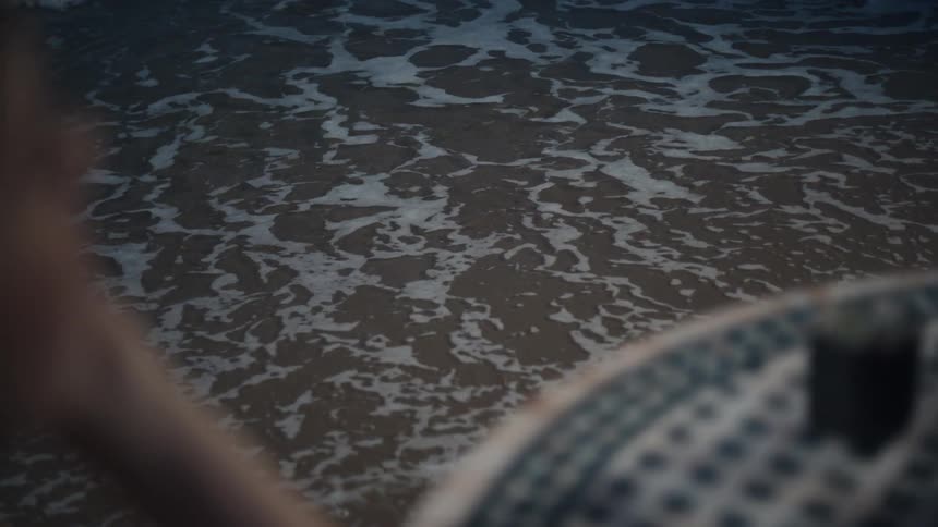 A woman sitting by the beachside watching the waves hit the shore at midday