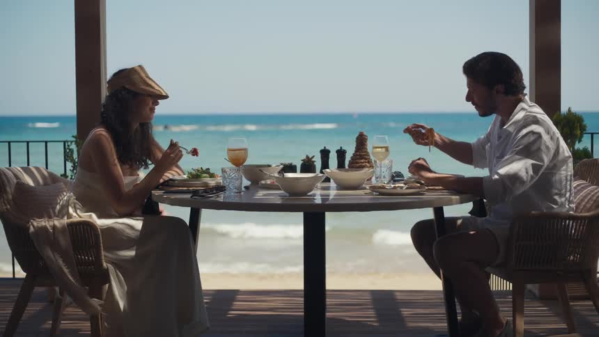 Couple having lunch at a seaside table with dishes and glasses of white wine overlooking the ocean