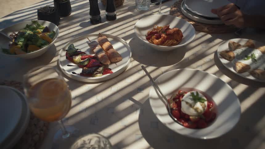 Table set with dishes of salad burrata with tomatoes bread with dip and grilled vegetables under light filtered by shadows