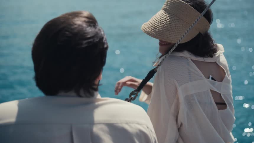 Woman smiling with a straw hat while talking to a man sitting by the blue sea
